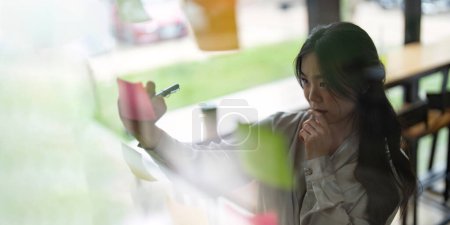 Foto de Joven mujer asiática frente al espejo mientras recoge lluvia de ideas en la oficina y la estrategia de trabajo. - Imagen libre de derechos