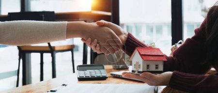 Foto de Agentes inmobiliarios y clientes se dan la mano para felicitar a la firma de un contrato para comprar una casa con tierra. - Imagen libre de derechos