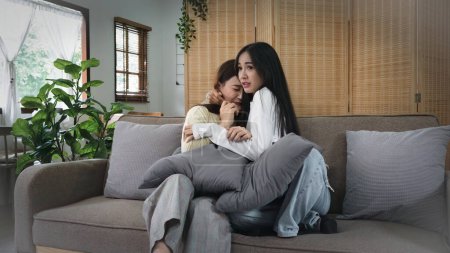 Téléchargez les photos : Homosexuel jeune femme lesbienne couple en pull assis sur canapé pour regarder le cinéma d'horreur effrayant tout en se câlinant dans le salon à la maison. - en image libre de droit