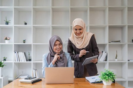 Téléchargez les photos : Deux femmes musulmanes asiatiques d'affaires utilisant ordinateur portable et tablette pour travailler ensemble dans le bureau, le respect et le concept de collaboration. - en image libre de droit