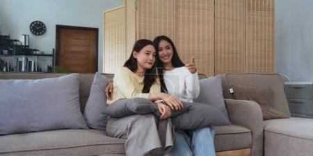 Foto de Asiática joven mujer homosexual lesbiana pareja poner en suéter sentado en sofá a ver cine en sala de estar en casa. - Imagen libre de derechos