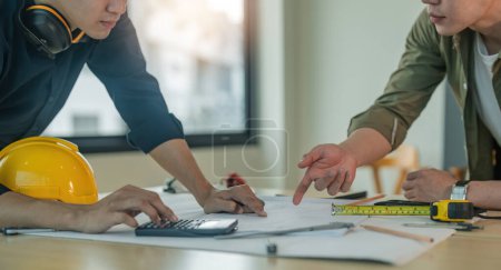 Photo for Closeup hand of engineer team with construction work plan discussion together blueprint on working table in construction site with safety helmet. - Royalty Free Image