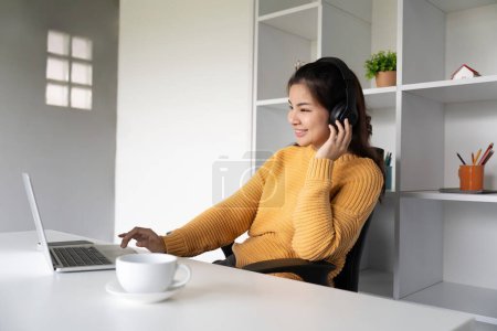 Photo for Asian woman using laptop at home and listening music on a headphones. - Royalty Free Image