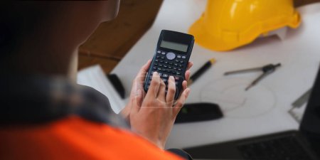 Photo for Closeup hand of engineer with construction work plan together blueprint on working table in construction site with safety helmet. - Royalty Free Image