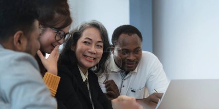Photo for Happy senior old korean businesswoman discussing statistics concept on laptop with african american indian and asian male colleague working together workplace, analyzing electronic documents. - Royalty Free Image