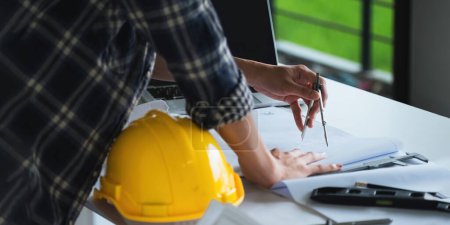 Photo for Closeup hand of engineer with construction work plan discussion together blueprint on working table in construction site with safety helmet. - Royalty Free Image
