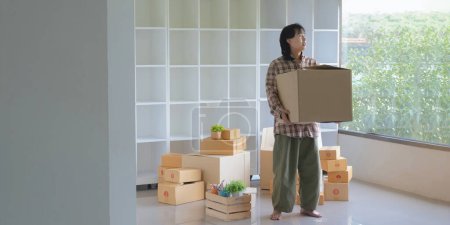Foto de Feliz hombre asiático llevando sus pertenencias arriba mientras se trasladan a un nuevo apartamento.. - Imagen libre de derechos