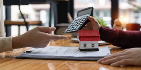 Foto de Agente inmobiliario con calculadora que presenta una tasa de interés de préstamo de vivienda al cliente. - Imagen libre de derechos