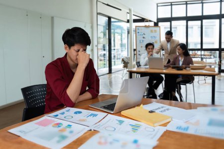 Téléchargez les photos : Les jeunes gens d'affaires asiatiques sont stressés en travaillant sur ordinateur portable ou dans la salle de réunion, Homme d'affaires fatigué avec des maux de tête au bureau, se sentant malade au travail. - en image libre de droit