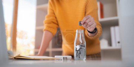 Foto de Contabilidad de negocios con el ahorro de dinero con la mano poner monedas en el concepto de vidrio de jarra financiera. - Imagen libre de derechos