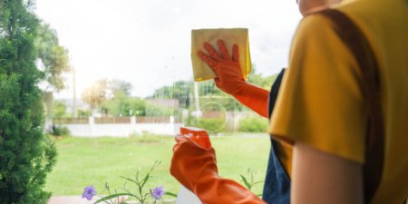 Téléchargez les photos : Jeune femme au foyer asiatique nettoyage vitre avec chiffons et pulvérisation de détergent, nettoyage maison le week-end. - en image libre de droit
