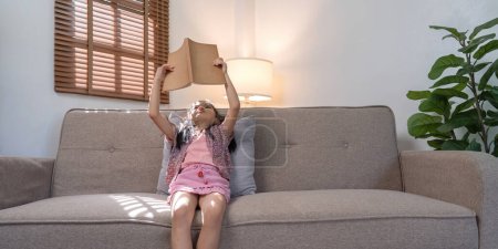 Foto de Niña asiática leer un libro sobre acogedor sofá en casa. - Imagen libre de derechos