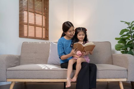 Photo for Mother and daughter read together on the sofa at home. - Royalty Free Image