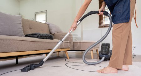 Photo for Asian woman cleaning in living room at home. Housekeeper or maid cleaner feel happy use vacuum cleaner to clean. - Royalty Free Image