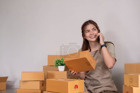 Photo for Asian woman holding parcel box and check order from cellphone. Online selling and online shopping concept. - Royalty Free Image