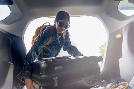 Téléchargez les photos : Femme asiatique concept de voyage prendre bagages valise et d'autres choses et appartenant à l'arrière de sa voiture tout en voyageant. - en image libre de droit