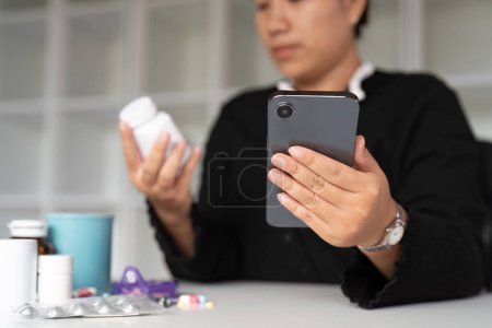 Foto de Cuidado de la salud mujer joven asiática que usa el teléfono inteligente para la prescripción de búsqueda en la medicina de la botella, texto de la etiqueta de la píldora sobre información en línea, efectos secundarios de instrucción, concepto de medicamento de farmacia. - Imagen libre de derechos
