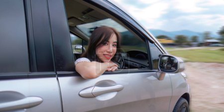 Téléchargez les photos : Jeune femme souriante garer la voiture à la voiture avant le voyage et souriant à la caméra. - en image libre de droit