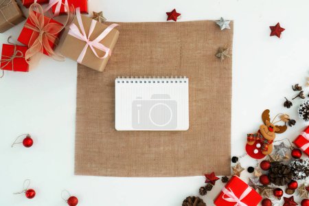 Photo for White tablecloth and notebook above of Christmas background design concept, holiday decoration ornament composition with Christmas gift box, star, reindeer. - Royalty Free Image