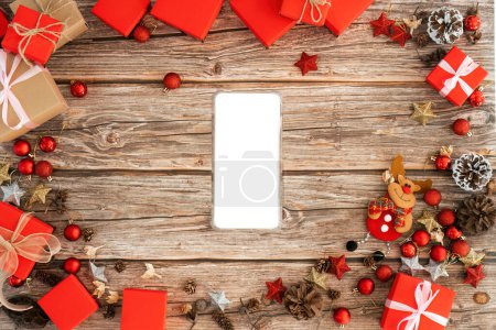 Photo for Top view above of Christmas background design concept, holiday decoration ornament composition with smartphone mockup Christmas gift box, star, reindeer with copy space isolated on wooden table. - Royalty Free Image