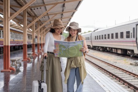 Foto de Concepto de viaje. amiga usar sombrero que sostiene mapa tienen bolsa y equipaje. mujer viajera esperando tren en la estación de tren. - Imagen libre de derechos