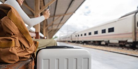 Foto de Mujer asiática viajera usando su teléfono inteligente móvil mientras espera un tren en una estación. - Imagen libre de derechos