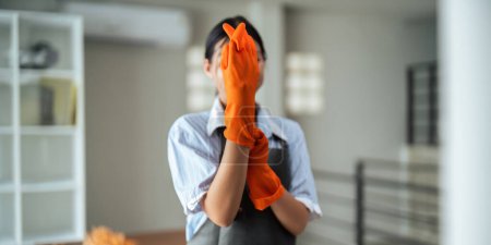 Foto de Primer plano de la empleada doméstica que se pone guantes de goma con productos químicos e instalaciones para ordenar la oficina de limpieza en el fondo. - Imagen libre de derechos