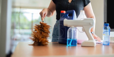 Photo for Asian woman cleaning in work room at home. Young woman housekeeper cleaner use feather duster wiping messy dirty for housekeeping housework. - Royalty Free Image