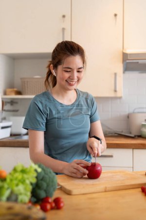 Photo for Woman asian cutting fruits and vegetable to prepare a smoothie while listening to music with earphones in the kitchen at home. - Royalty Free Image