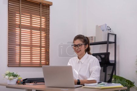 Foto de Retrato de hermosa joven mujer de negocios asiática sentado en la oficina moderna estación de trabajo y mecanografía en el ordenador portátil. - Imagen libre de derechos