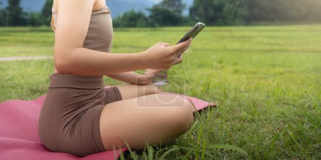 Téléchargez les photos : Femme asiatique regardant son smartphone et lisant sur look sport application au parc. - en image libre de droit