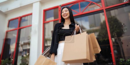 Photo for Happy beautiful young stylish woman with shopping bag while walking come out of mall on holiday Black Friday. - Royalty Free Image