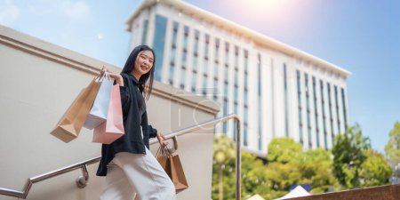 Foto de Feliz hermosa mujer con estilo joven con bolsa de compras mientras camina salir del centro comercial de vacaciones Viernes Negro. - Imagen libre de derechos