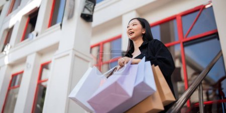 Photo for Happy beautiful young stylish woman with shopping bag while walking come out of mall on holiday Black Friday. - Royalty Free Image