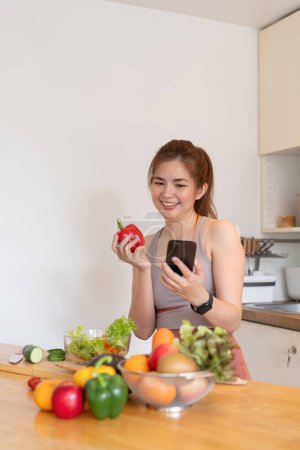 Téléchargez les photos : Heureux sourire asiatique féminin manger des légumes fruits et en utilisant un smartphone, alimentation jour de compter les calories. concept d'alimentation et de soins de santé. - en image libre de droit