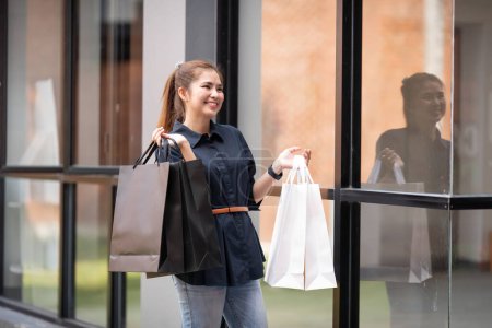 Foto de Feliz hermosa mujer con estilo joven con bolsa de compras mientras camina cerca del centro comercial de vacaciones Viernes Negro. - Imagen libre de derechos