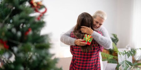 Téléchargez les photos : Fille donnant cadeau à la mère heureuse et embrasser à l'intérieur à la maison à Noël. - en image libre de droit