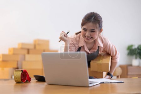 Téléchargez les photos : Femme entrepreneur asiatique préparer boîte de colis et vérifier la commande en ligne sur ordinateur portable pour la livraison de contrôle commercial. marketing en ligne, boîte d'emballage, vendeur PME. concept d'entreprise en démarrage. - en image libre de droit