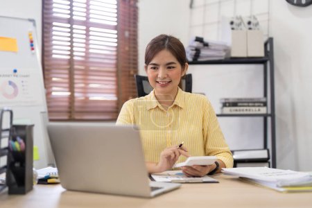 Téléchargez les photos : Jeune femme d'affaires asiatique assis au bureau avec des données et un graphique en utilisant la calculatrice finance analyse comptable, plan et stratégie d'amélioration des affaires. - en image libre de droit