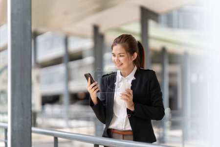 Photo for Young Asian business woman wearing suit using application on cell phone, read news on smartphone, fast connection, checking mobile apps outdoors. - Royalty Free Image