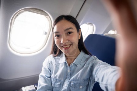 Photo for Travel and technology. Young woman asian in plane taking selfie while sitting in airplane seat. - Royalty Free Image