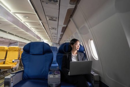 Téléchargez les photos : Voyager et technologie. Voler en première classe. Jolie jeune femme d'affaires asiatique utilisant un ordinateur portable tout en étant assis dans l'avion. - en image libre de droit