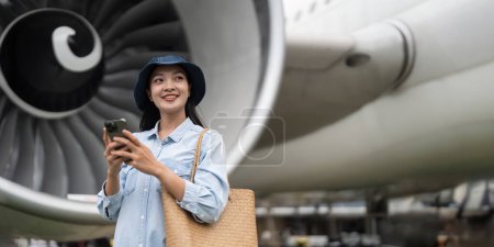 Foto de Viajes y tecnología. Bonita joven asiática usando smartphone a la espera de embarcar en terminal del aeropuerto. - Imagen libre de derechos