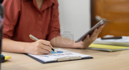 Téléchargez les photos : Femme d'affaires avec tablette numérique résumé financier graphique assis au bureau. jeune femme analyse tableau d'investissement dans le bureau. - en image libre de droit