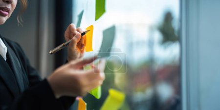 Photo for Young creative business woman Asian using sticker note in glass wall to writing strategy business plan to development growth to success. - Royalty Free Image