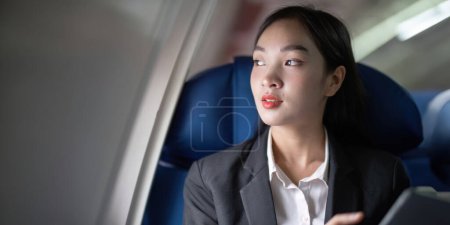 Foto de Exitosa mujer de negocios asiática, mujer de negocios que trabaja en cabina de avión durante el vuelo en tableta. - Imagen libre de derechos