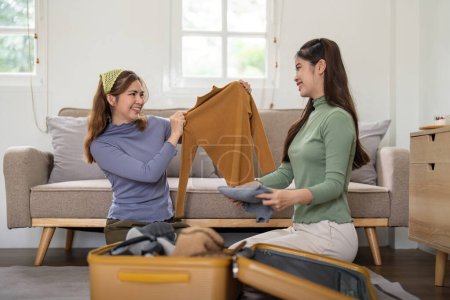 Photo for Asian woman prepare to pack clothes travel places with her friends. Asian beautiful two women friend pack things in your travel bag for holidays for her vacation trip. - Royalty Free Image
