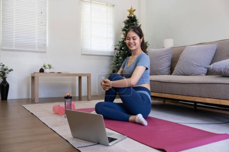 Photo for Young Asian sporty fitness woman coach do practice video online training yoga laptop in living room at home. - Royalty Free Image