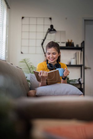Photo for Happy young woman read book on sofa at home. Lifestyle freelance relax in living room. lifestyle relaxation concept. - Royalty Free Image