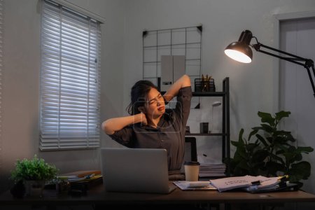 Foto de Asiática mujer de negocios tienen un dolor de cuello porque el uso de la computadora portátil y trabajar durante mucho tiempo por la noche. - Imagen libre de derechos